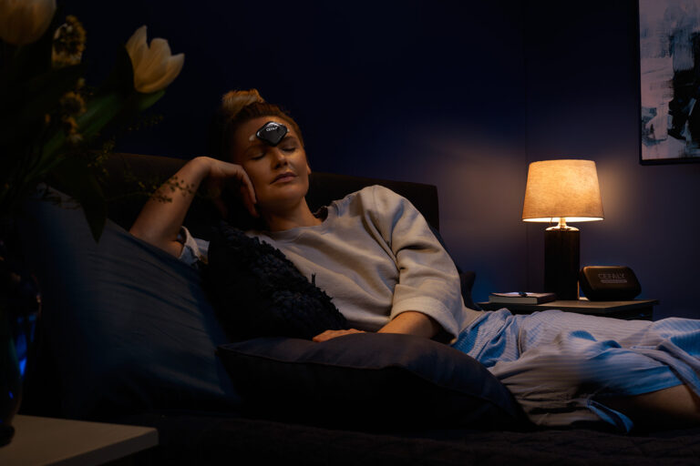 a relaxed woman laying on a bed wearing a CEFALY device on her forehead