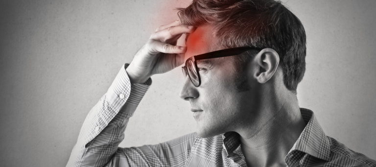 a black and white filtered image of a man wearing glasses clutching his forehead as he is experiencing a migraine, which is indicated by a red circle