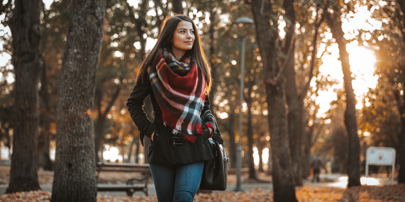 a woman wearing a plaid scarf is walking through a park