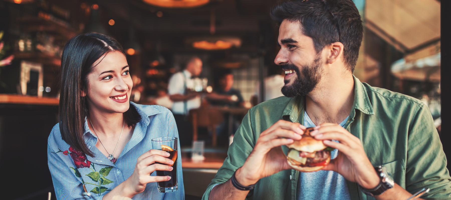 a man and a woman are sitting at a table eating hamburgers and drinking soda