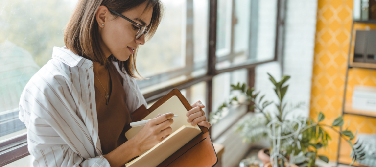 a woman wearing glasses is writing in a notebook