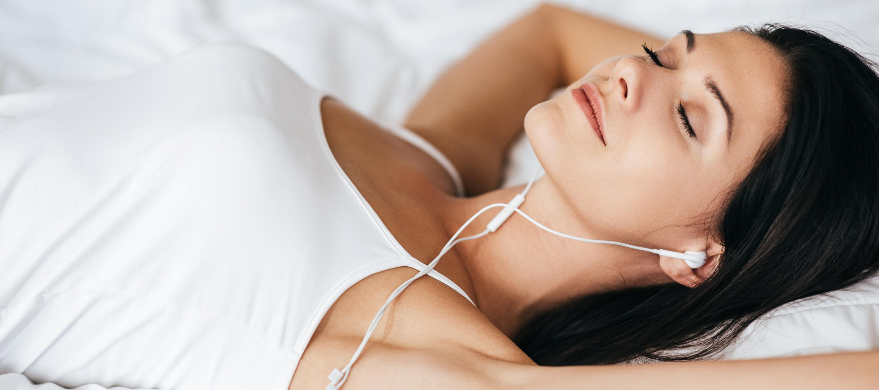 a smiling woman laying on a bed wearing earbuds with her eyes closed