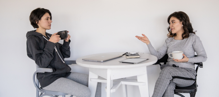 two women sit at a table drinking coffee and talking