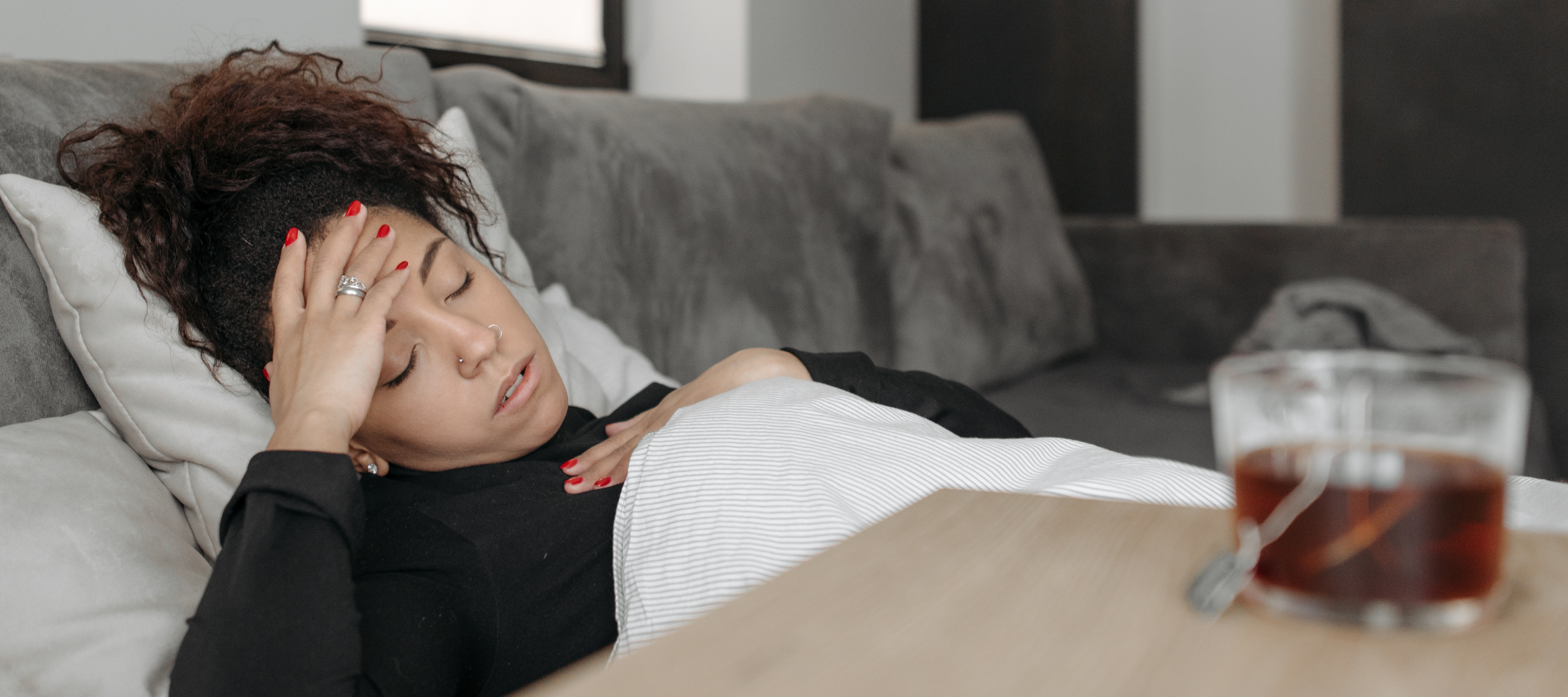 a woman in pain is laying in bed with her hand on her forehead next to a cup of tea on her nightstand