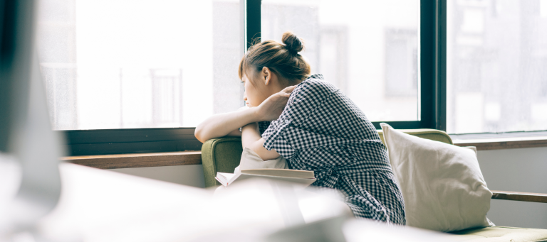 a woman sitting on a couch looking out a window with a book balanced on her lap