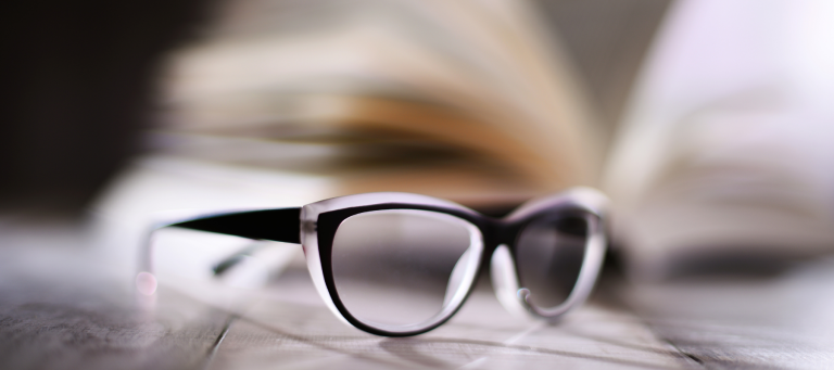 a pair of glasses sits on a table in front of an open book