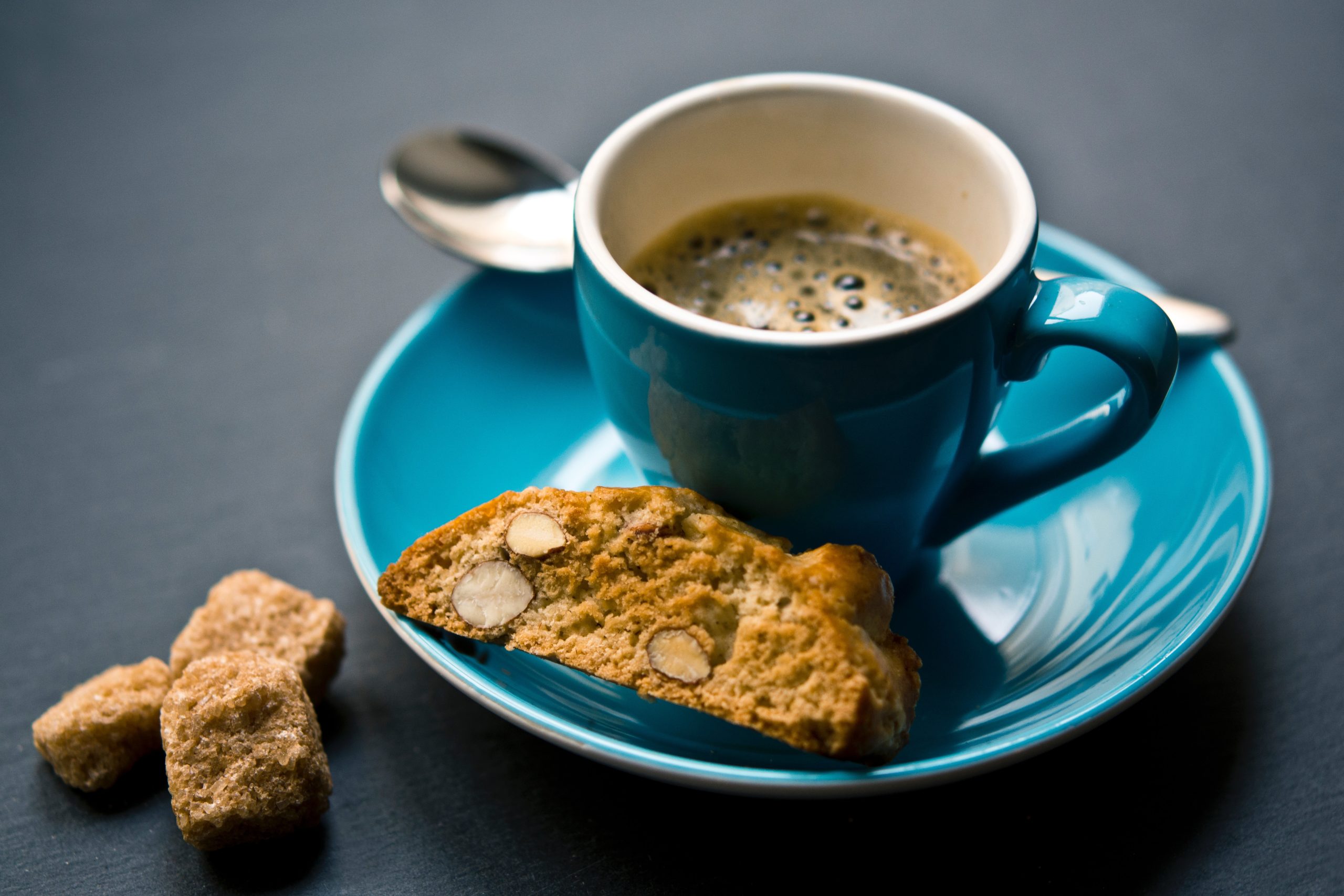 a cup of coffee sits on a blue saucer next to a pastry