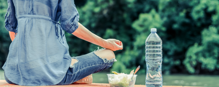 a woman sits outside with her legs crossed next to a bottle of water and a salad