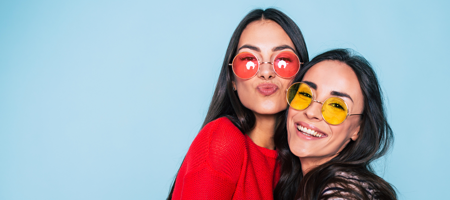 two women wearing colored sunglasses are smiling