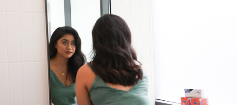 a woman looks at her reflection in a bathroom mirror