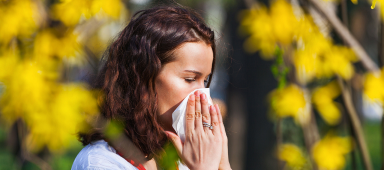 a woman blowing her nose in front of a tree with yellow flowers