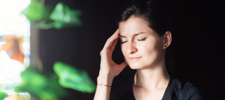 a woman with her eyes closed holds her hand to her forehead because of a migraine