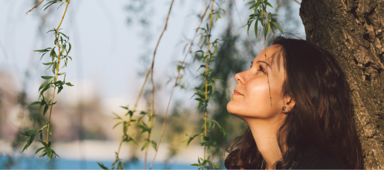 a woman leaning against a tree looking up