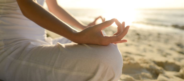 a woman meditates on the beach with her hands in a lotus position